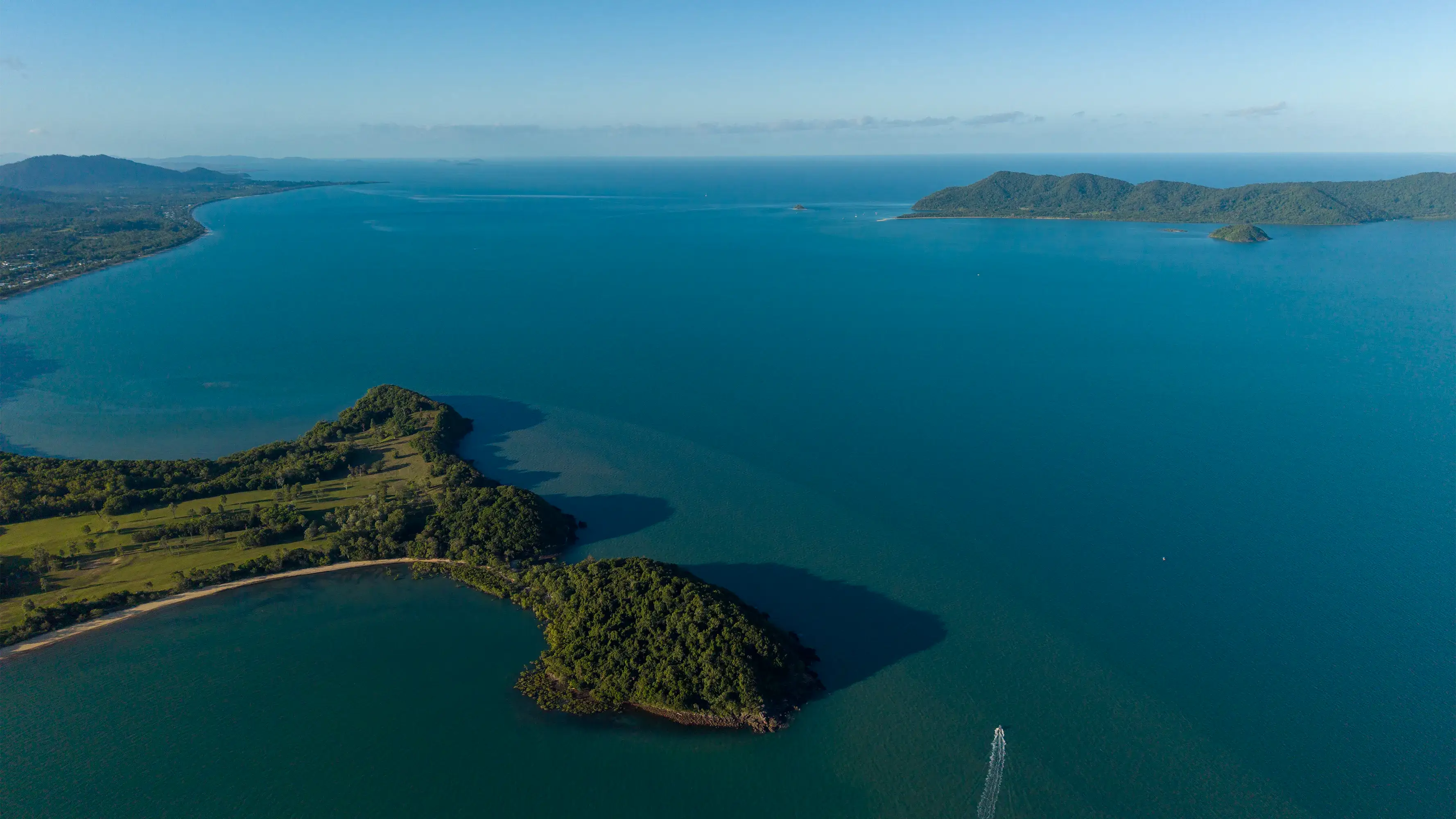 A boat heading out past the forested tip of the Point, an island across the water